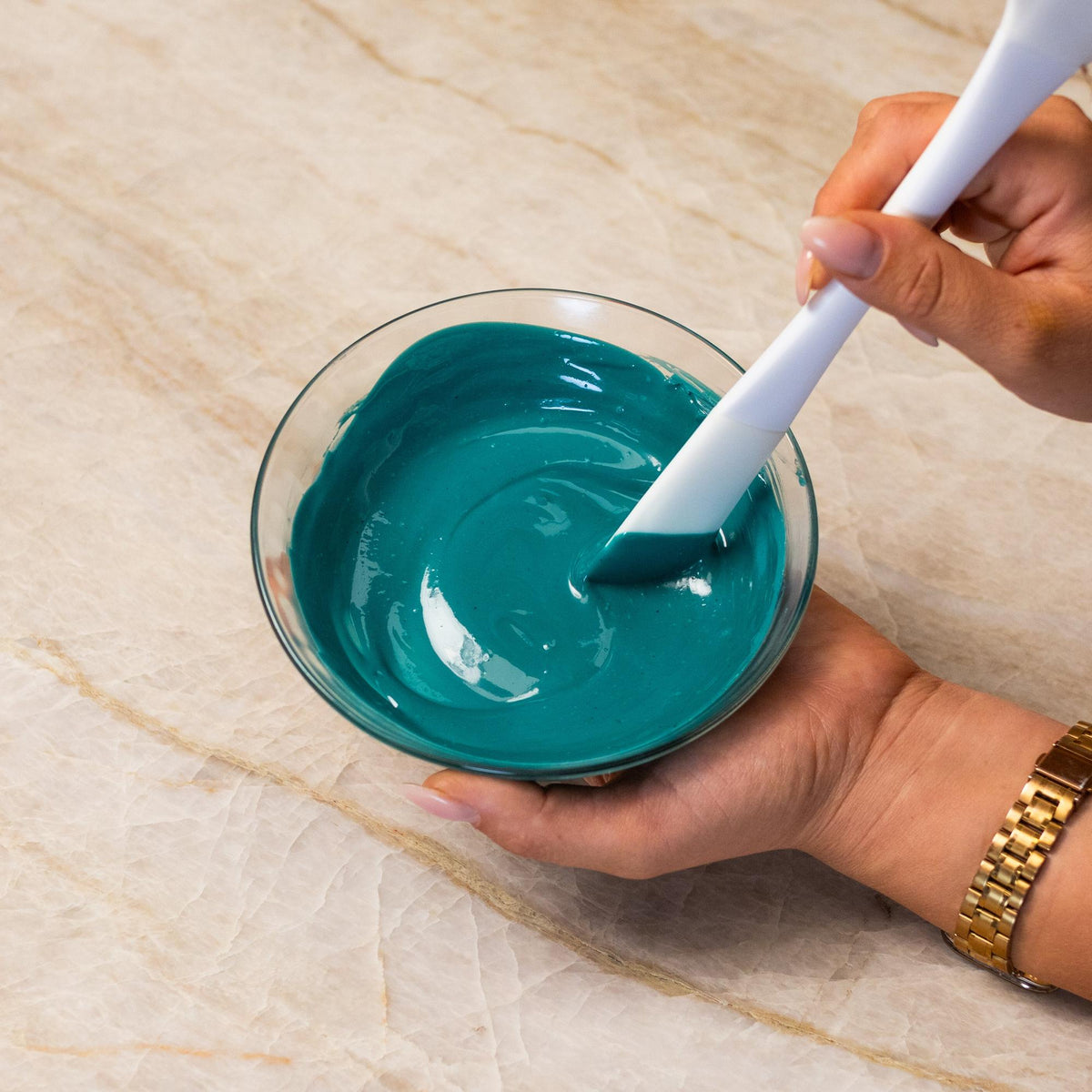 Teal chocolate mixed with natural food coloring powder in a bowl.