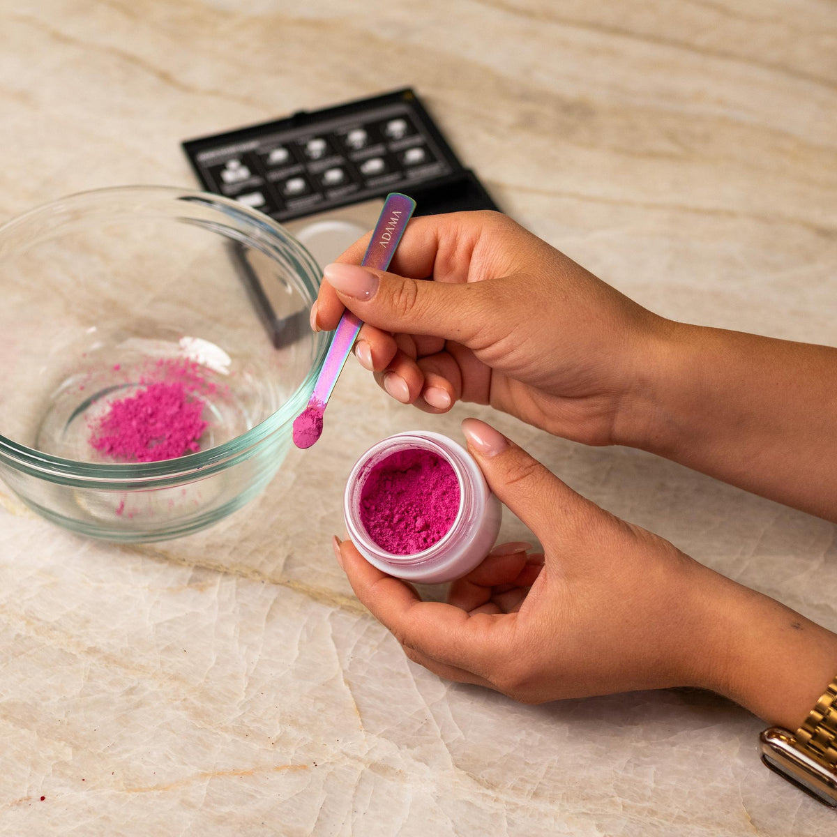 Pink natural food coloring powder being added to glass bowl with a measuring spoon.