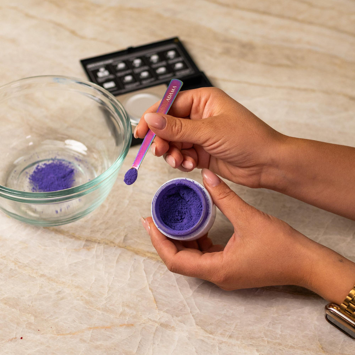 Purple natural food coloring powder being added to glass bowl with a measuring spoon.