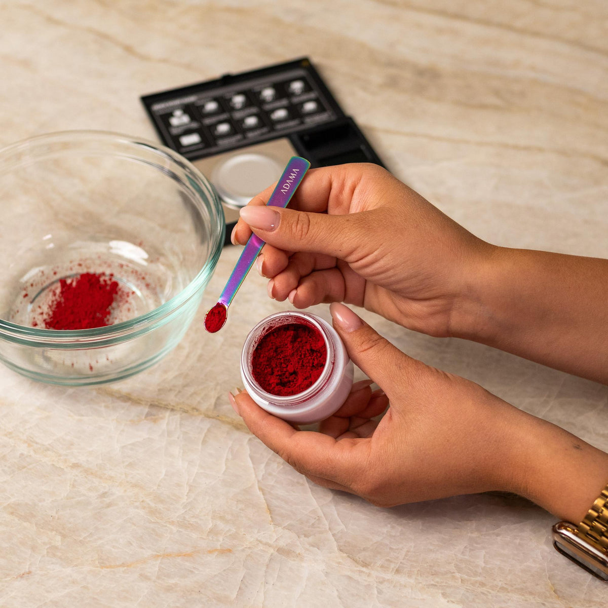 Red natural food coloring powder being added to glass bowl with a measuring spoon.