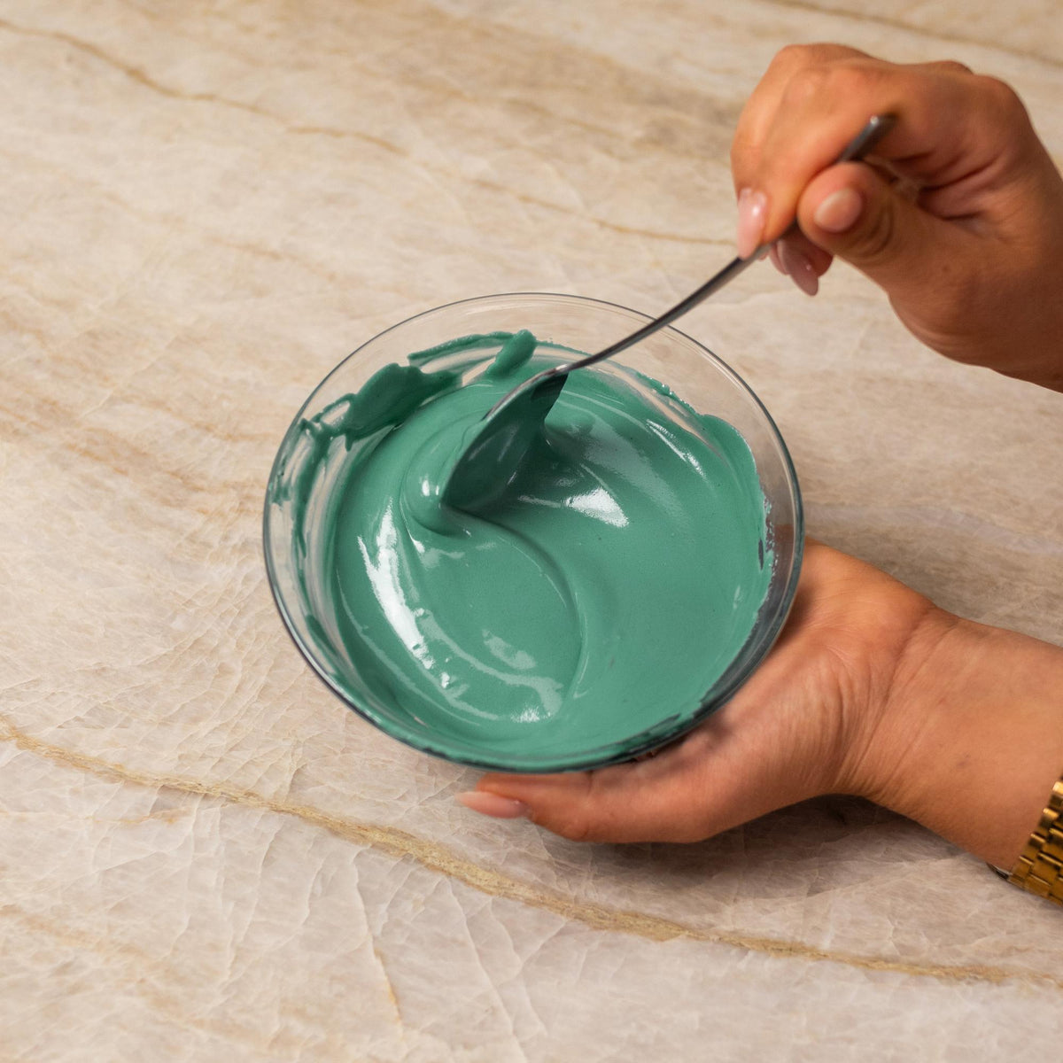 Teal frosting mixed with natural food coloring powder in a bowl.