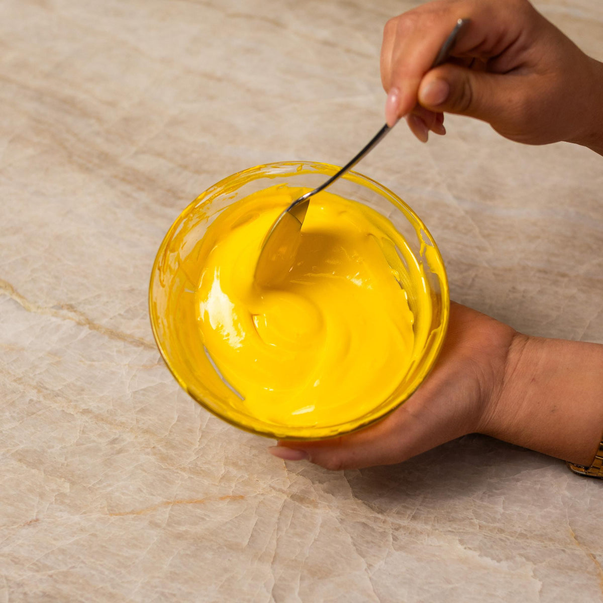 Yellow frosting mixed with natural food coloring powder in a bowl.