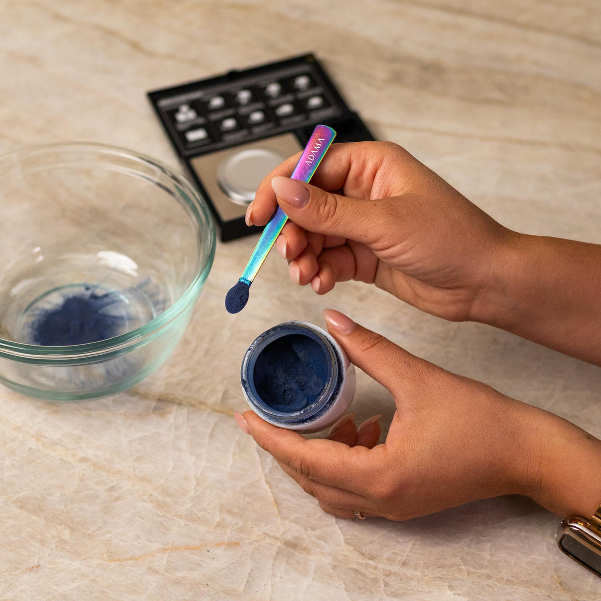 Green natural food coloring powder being added to glass bowl with a measuring spoon.