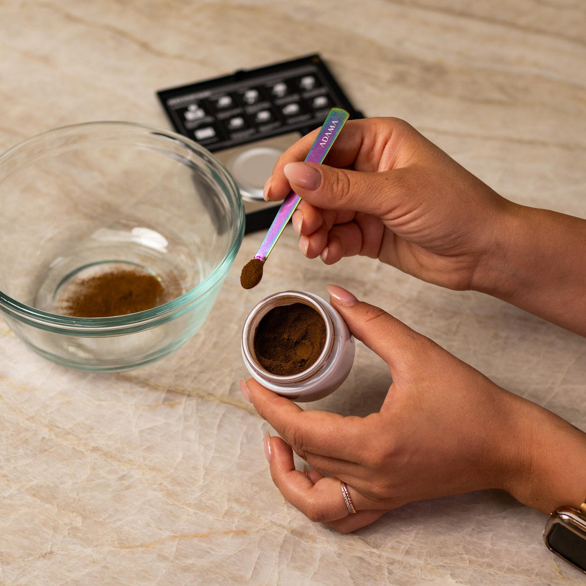 Red natural food coloring powder being added to glass bowl with a measuring spoon.