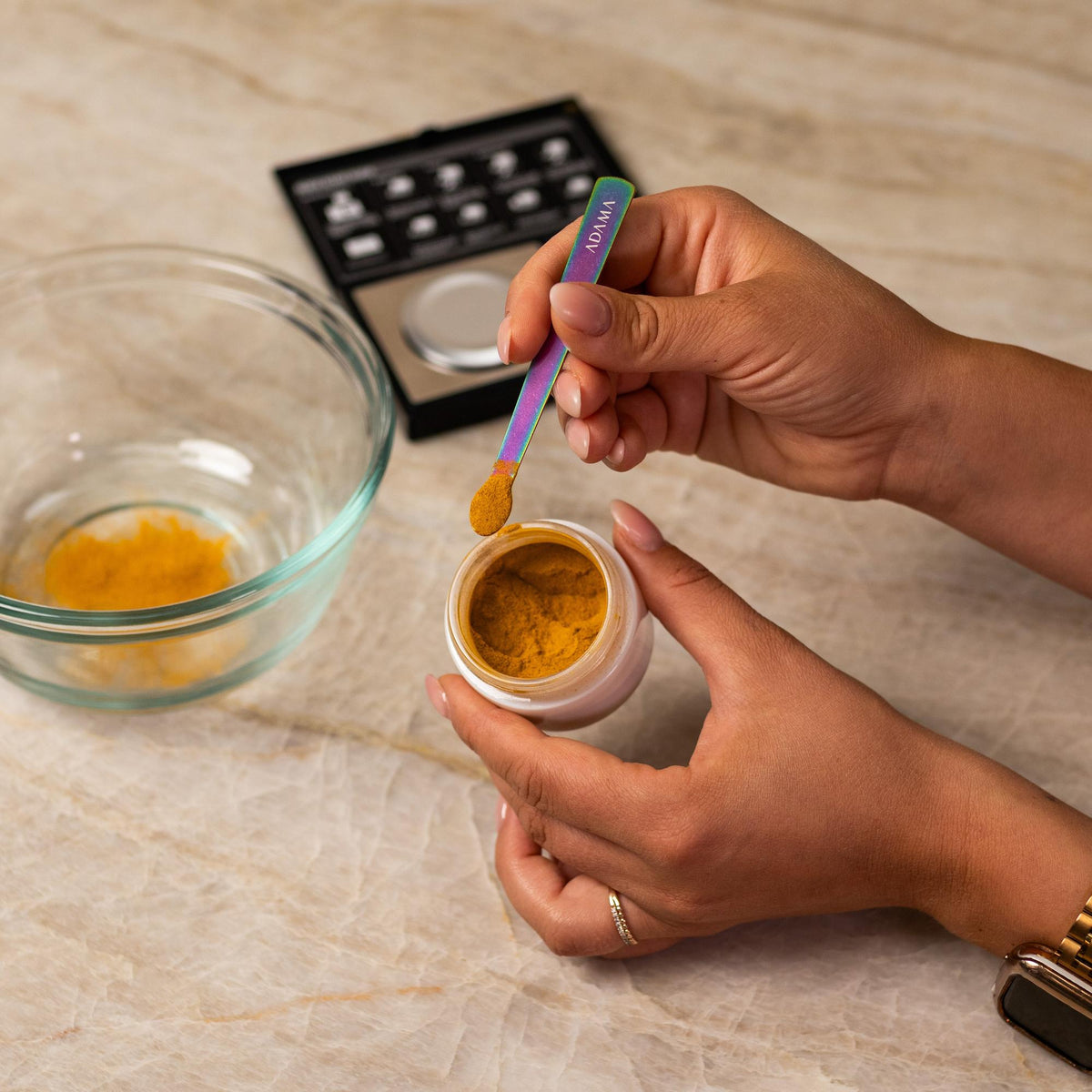 Orange natural food coloring powder being added to glass bowl with a measuring spoon.