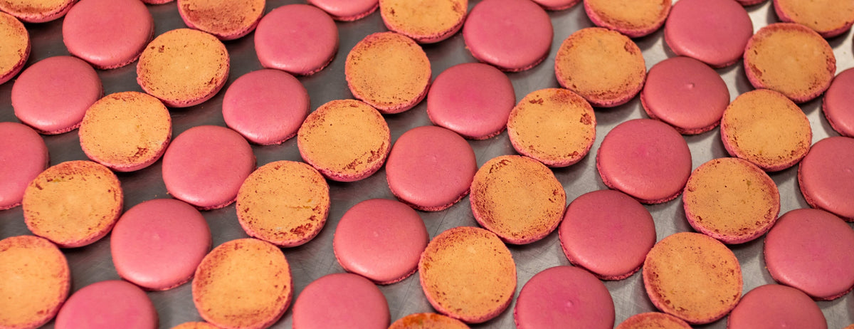Rows of vibrant pink macaron shells on a stainless table.
