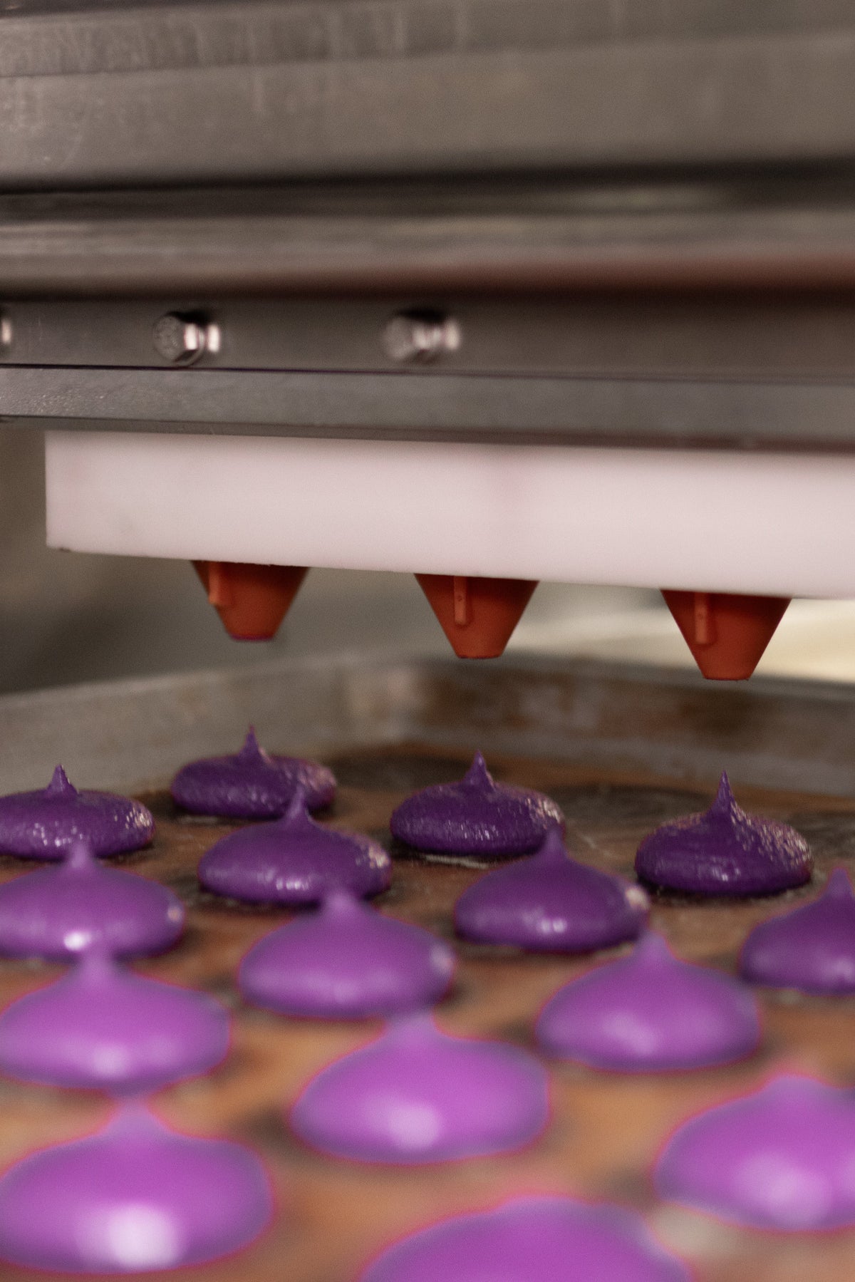 Machine piping macaron batter into shells during bake testing for purple ADAMA natural food coloring.