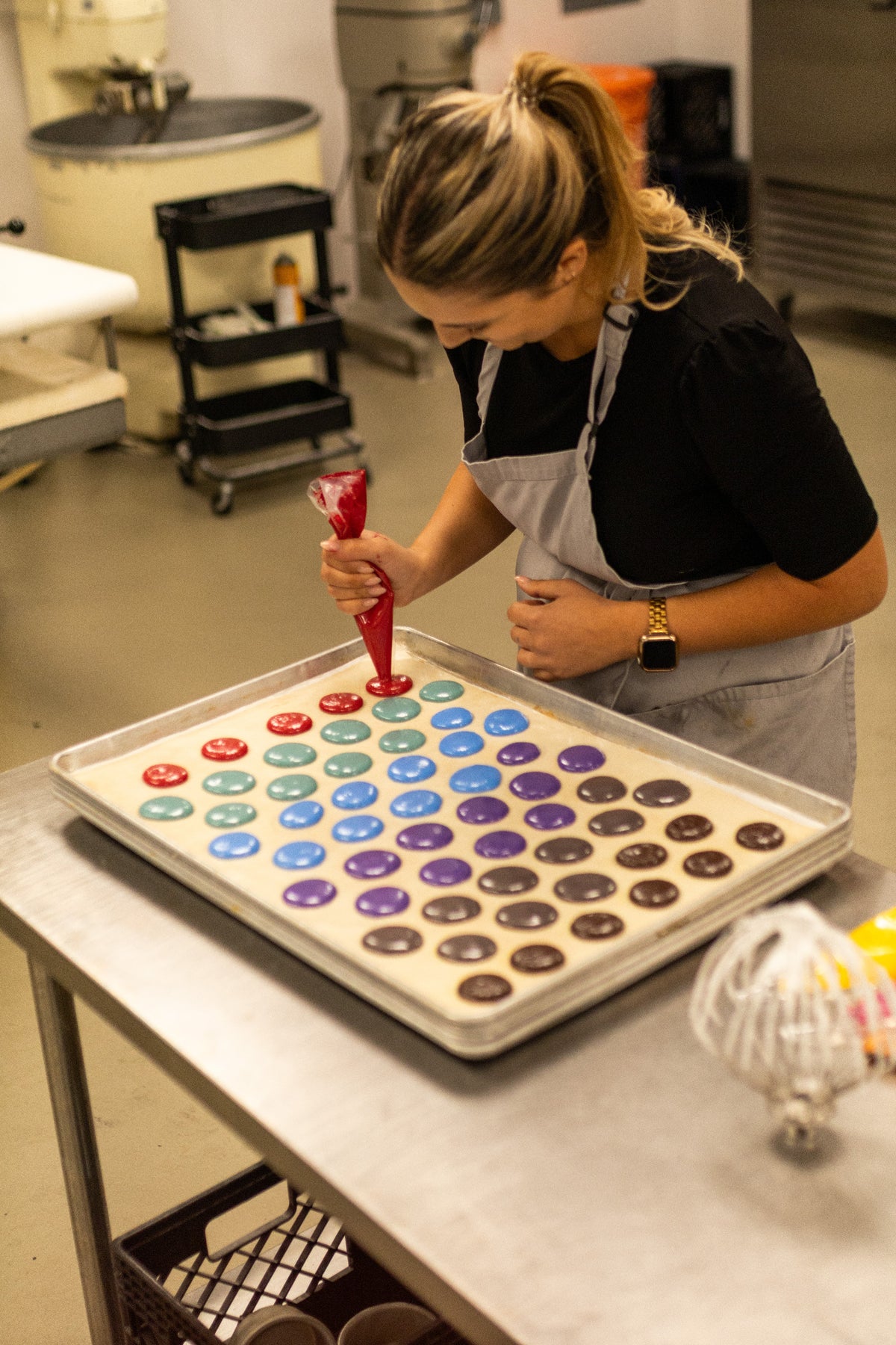 Baker piping colorful macaron shells while testing ADAMA natural food coloring.