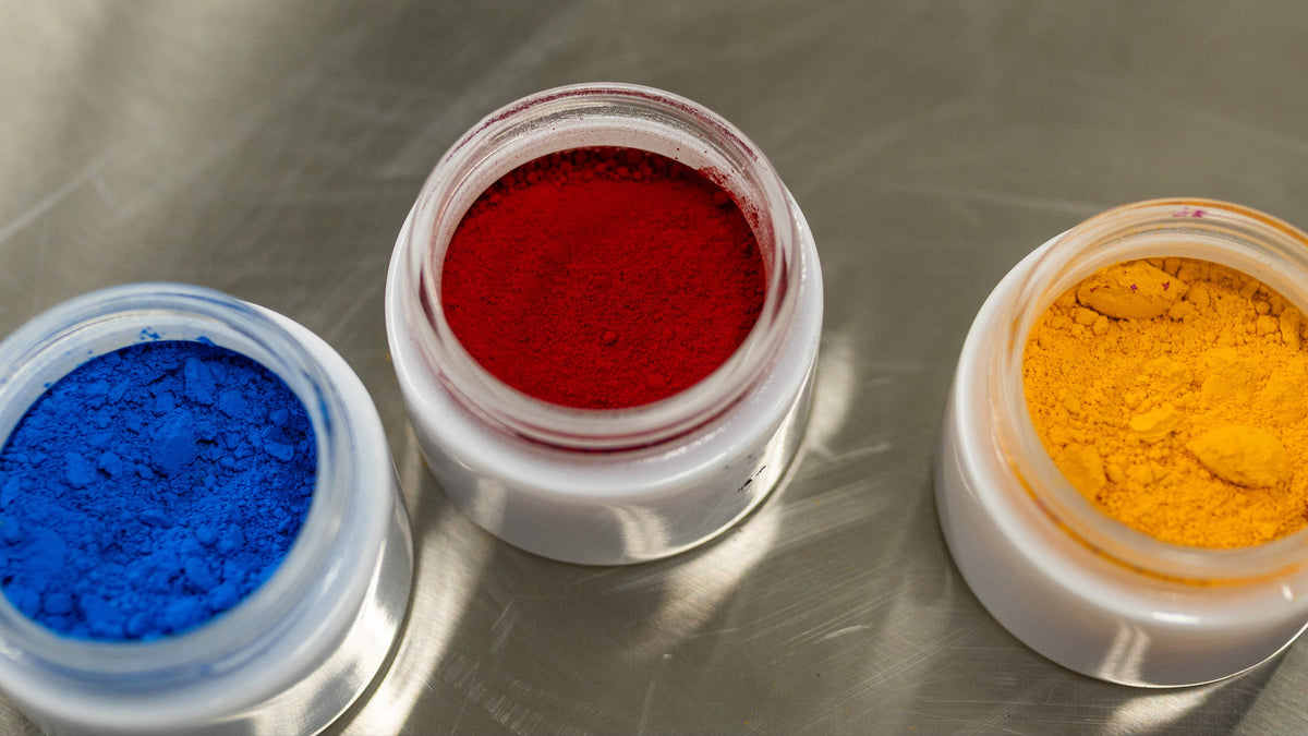 Blue, red, and yellow ADAMA natural food coloring powders in open containers.