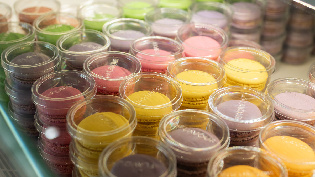 Colorful macarons packaged in clear containers for commercial bakery production