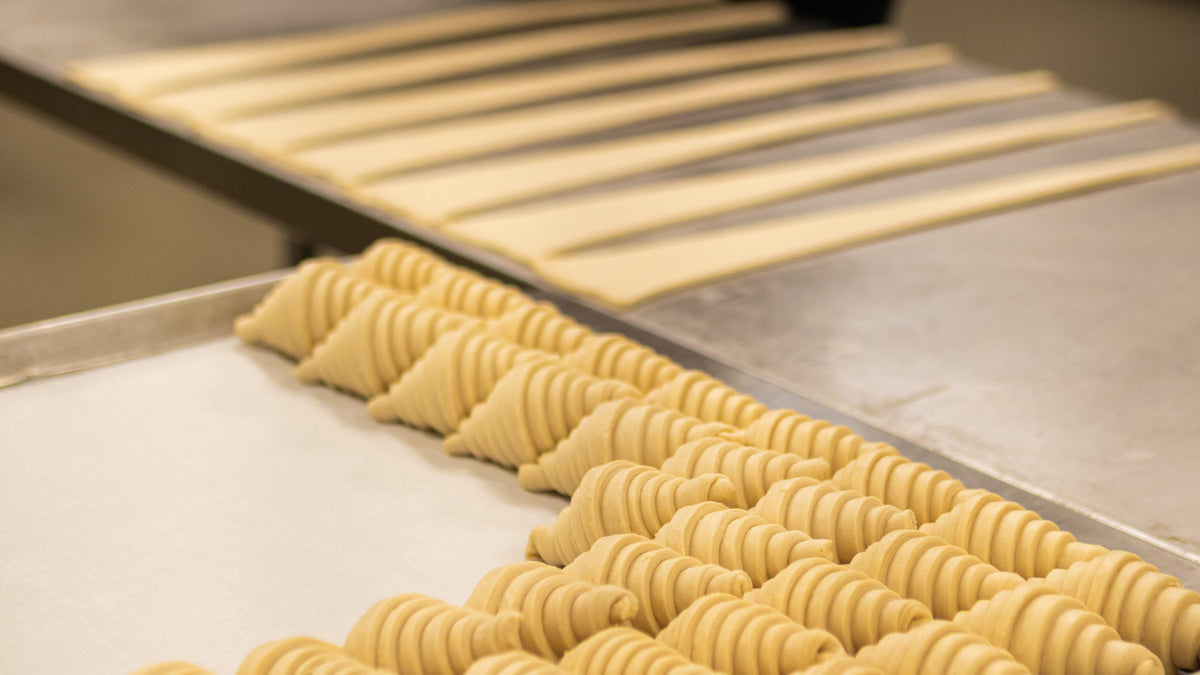 Raw dough croissants being prepared for baking inside a professional kitchen.