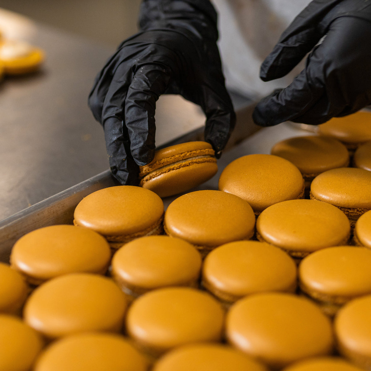 Vibrant orange macarons being prepared for packaging in a professional kitchen.