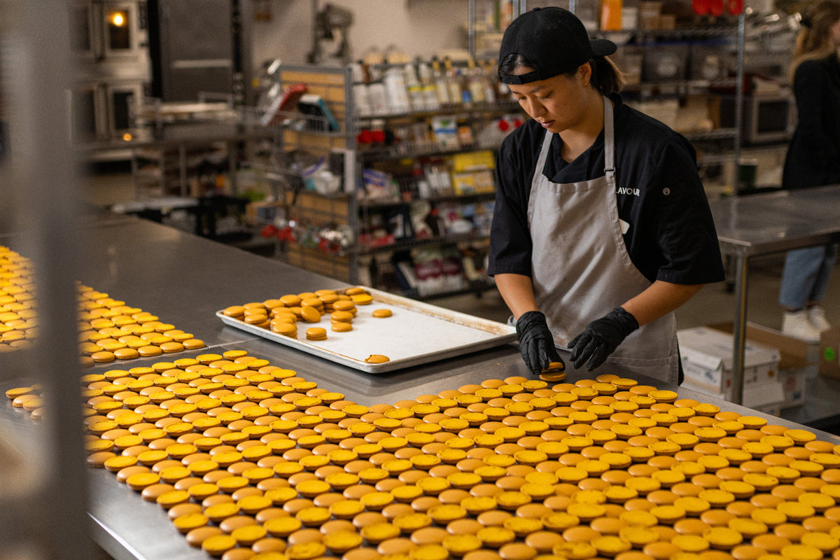 Baker laying out vibrant orange macaron shells made with ADAMA natural food coloring.