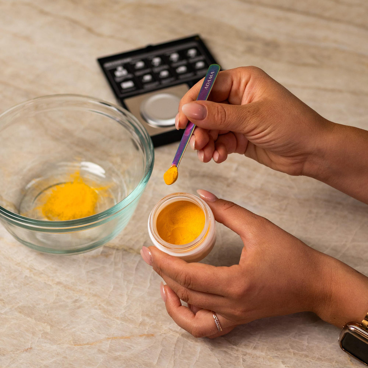 Yellow natural food coloring powder being added to glass bowl with a measuring spoon.