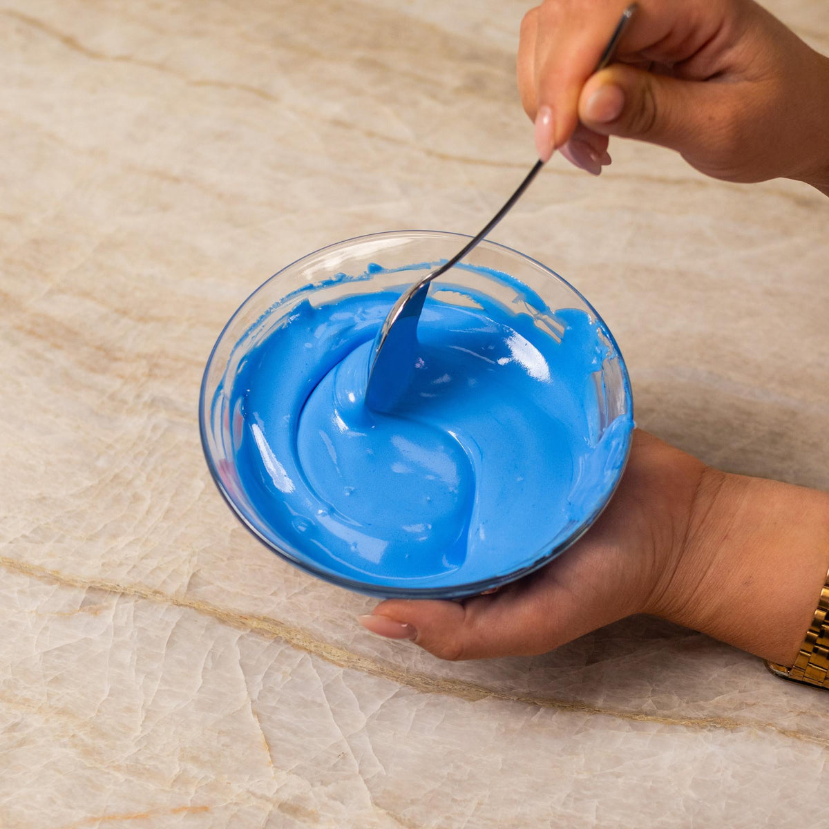 Blue frosting mixed with natural food coloring powder in a bowl.