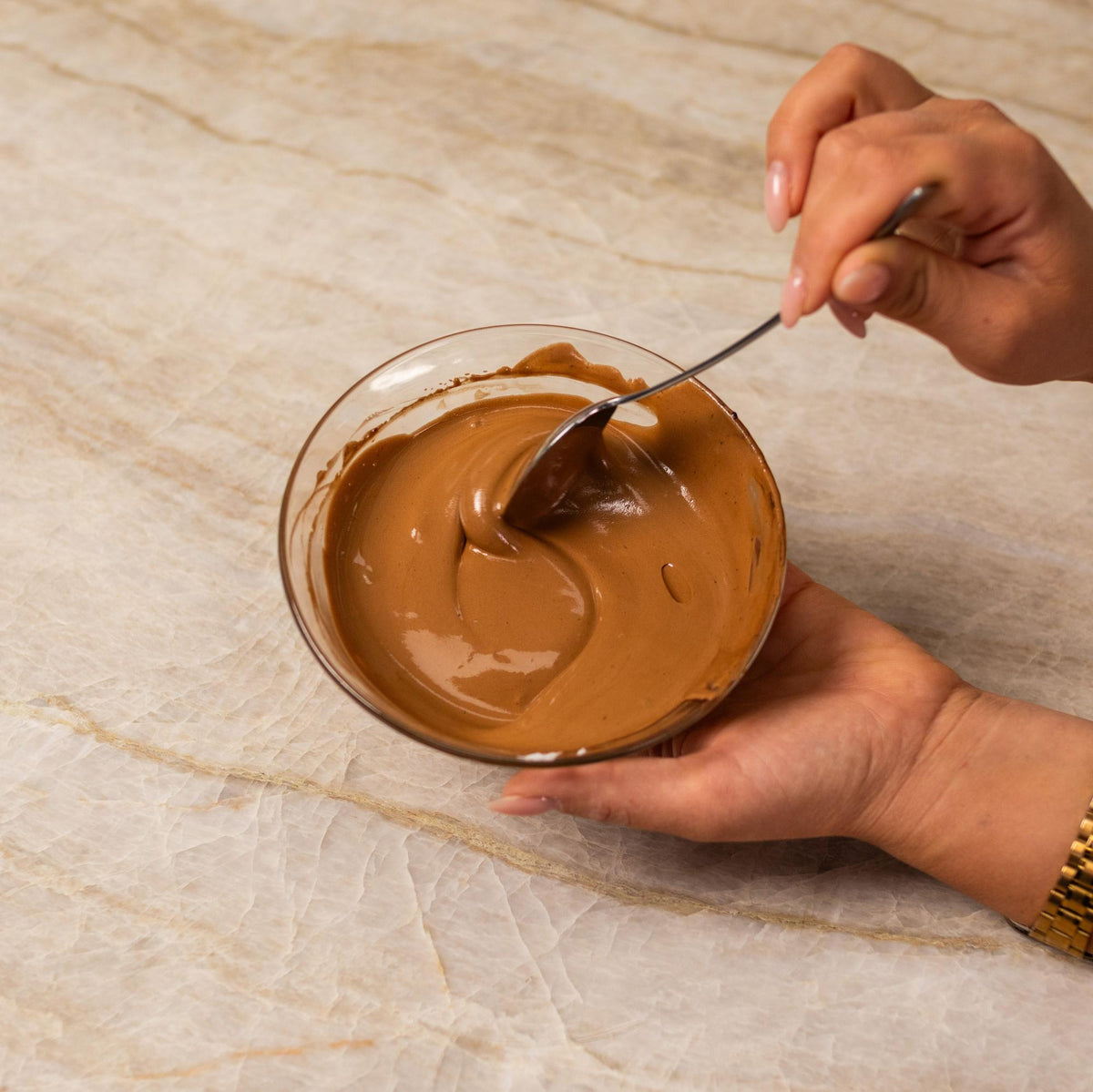 Brown frosting mixed with natural food coloring powder in a bowl.