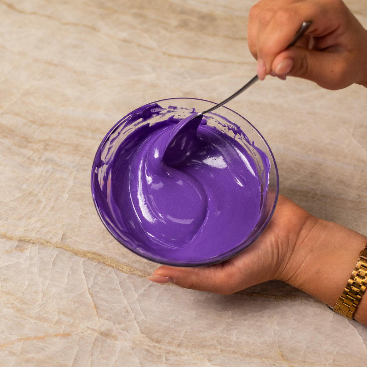Purple frosting mixed with natural food coloring powder in a bowl.