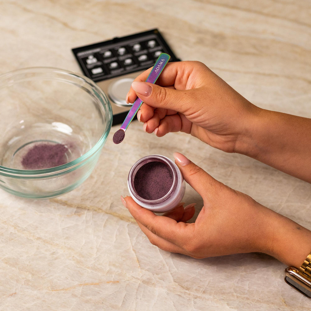 Pink natural food coloring powder being added to glass bowl with a measuring spoon.
