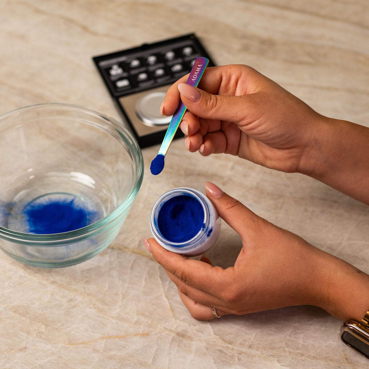 Purple natural food coloring powder being added to glass bowl with a measuring spoon.