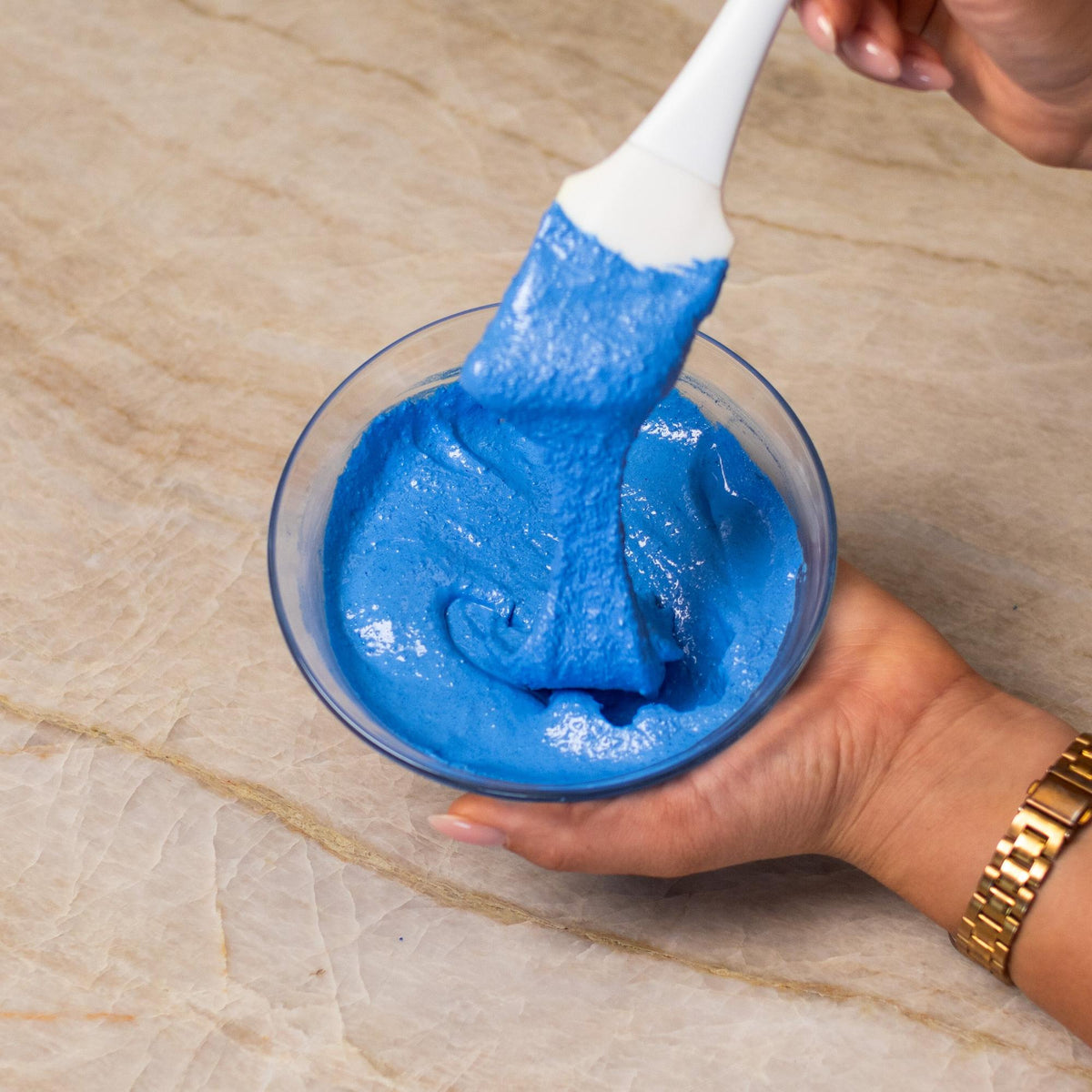 Blue macaron batter mixed with natural food coloring powder in a bowl.