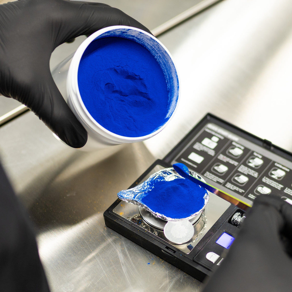 Blue natural food coloring powder being weighed on a digital scale during product testing.