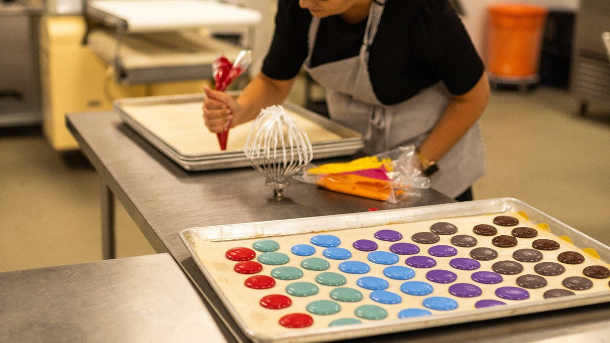 Baker piping colorful macaron shells during ADAMA natural food coloring testing.
