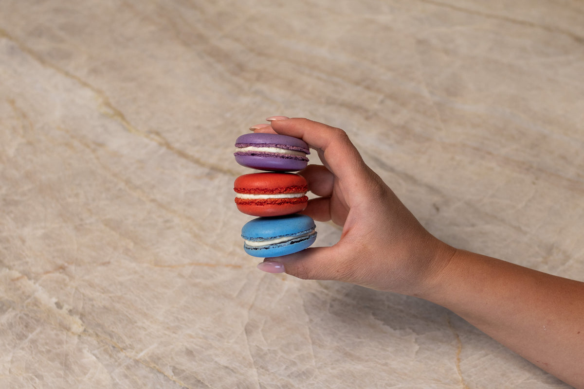 Purple, red, and blue macarons made with ADAMA natural food coloring held in a hand.