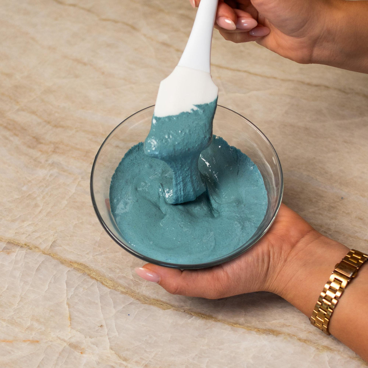 Teal macaron batter mixed with natural food coloring powder in a bowl.