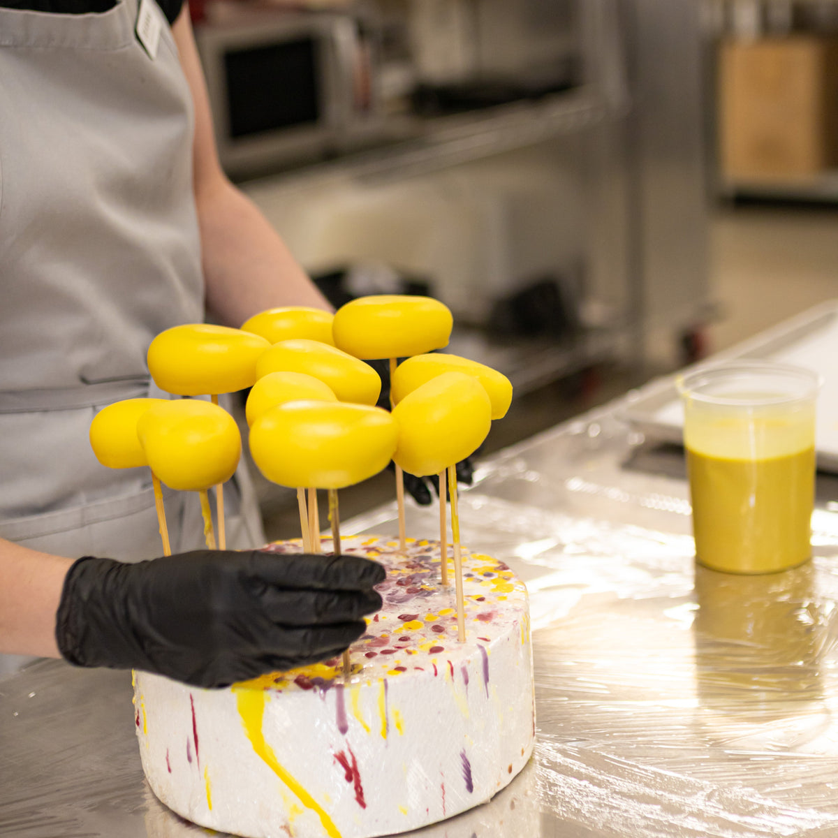 Baker dipping yellow mousse cakes made with ADAMA natural food coloring in a professional kitchen.